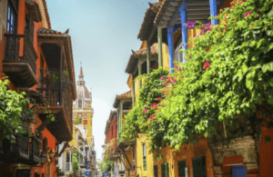 Colorful colonial street in Cartagena, Colombia, with balconies draped in bougainvillea and a cathedral tower in the distance