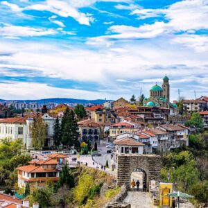 Historic Bulgarian town with terracotta rooftops, a domed church, and stone archway gate under a blue sky