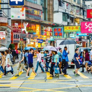 Pedestrians with umbrellas crossing a busy Hong Kong street lined with colorful storefront signs